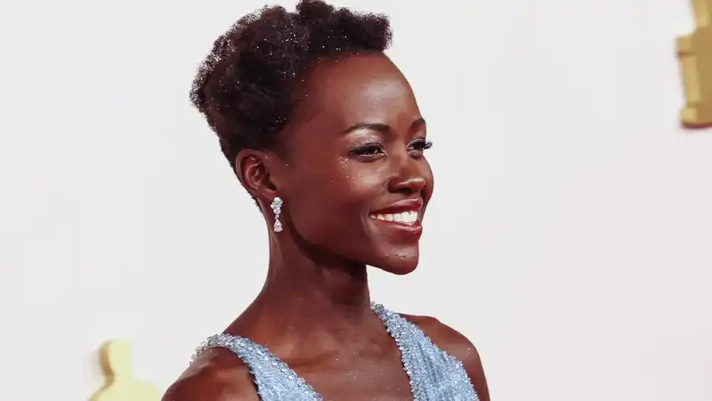 Lupita Nyong'o walks the Oscar red carpet coated in a shimmering silver glow.