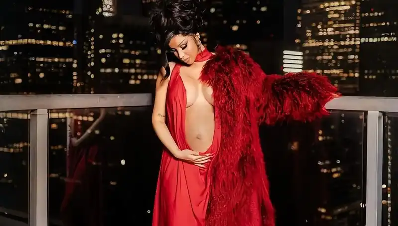 Cardi B reveals her third pregnancy in a red gown and fur coat that reveals her belly.